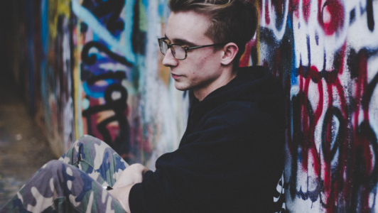 Young person sitting against graffitied wall, therapy for anxiety, how we can help